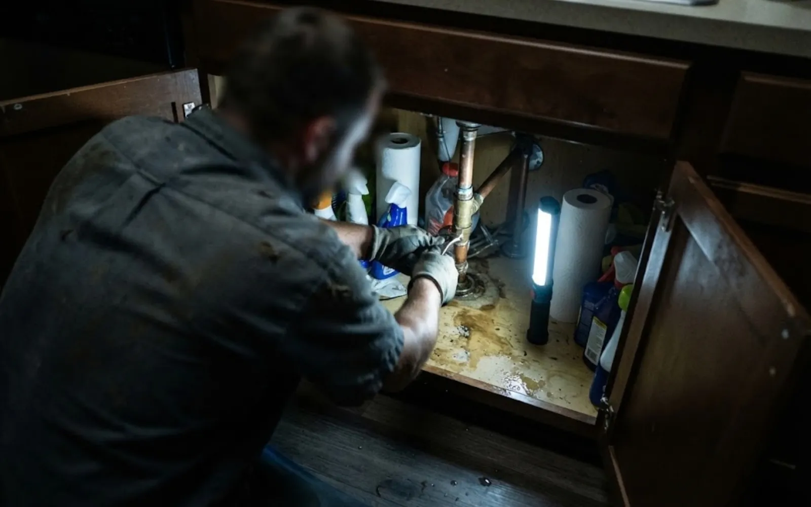 plumber repairing a leaking pipe under a kitchen sink