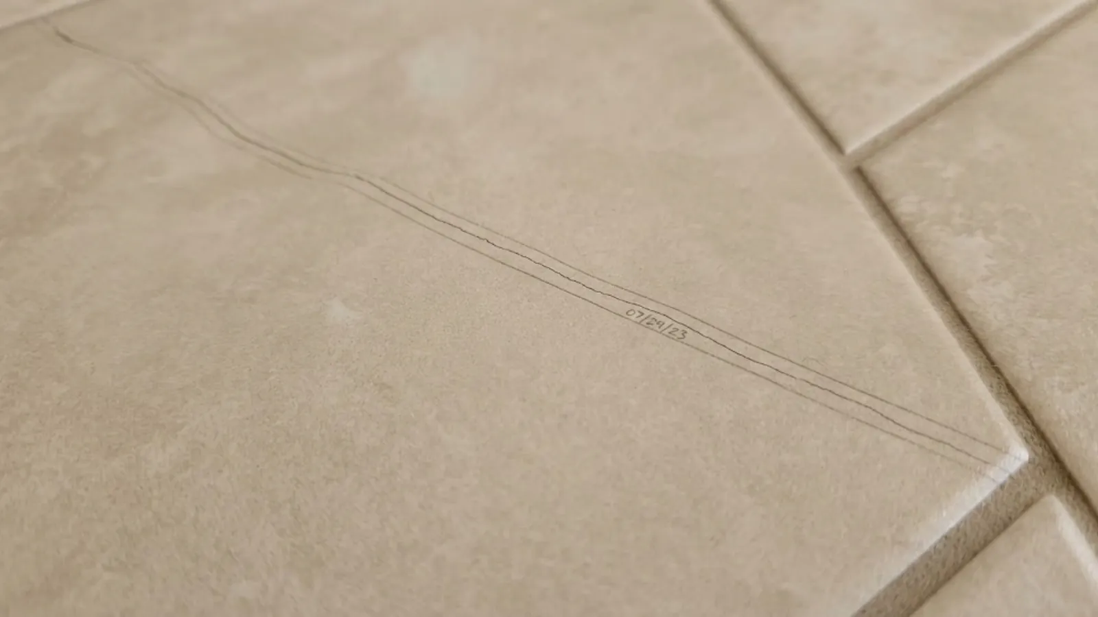 crack in a tile floor marked with pencil and a date